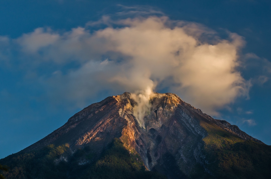 Una montaña con una columna de humo o vapor elevándose de su cima.