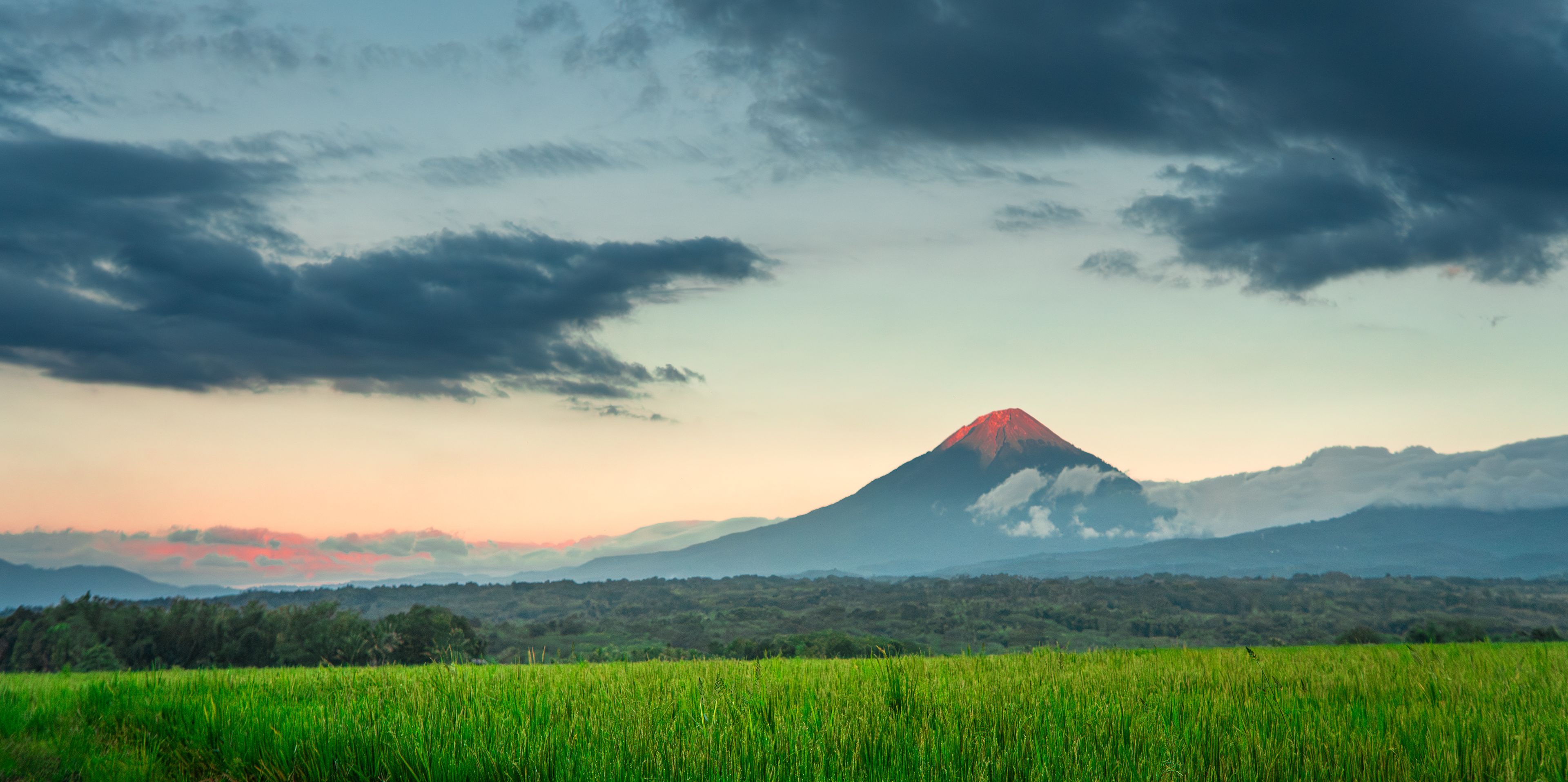 Beautiful landscape of Mount Inerie volcano with clouds at dusk, overlooking vibrant green rice paddies in Bajawa, Flores, Indonesia.
