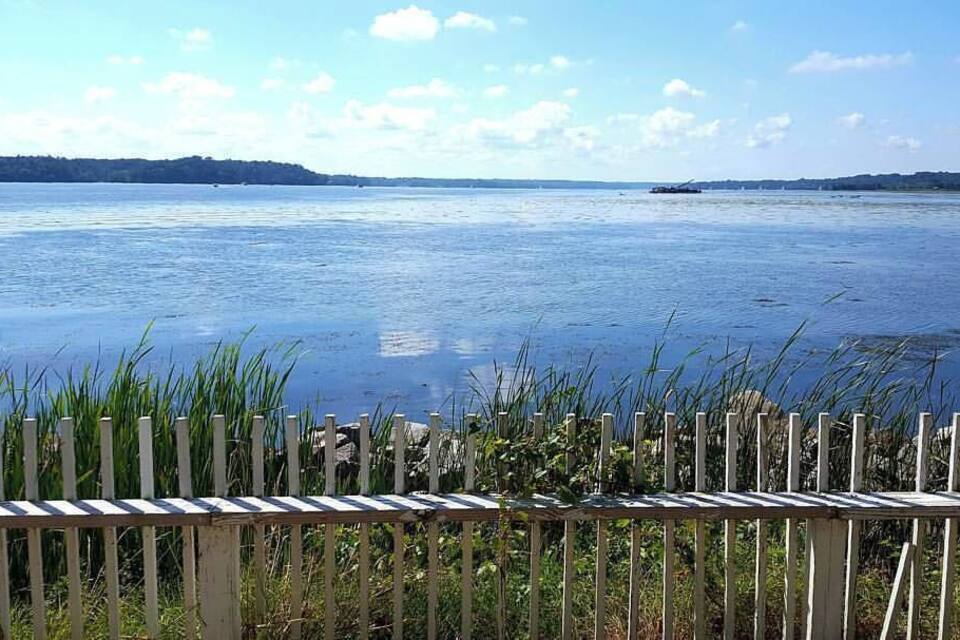 A calm lake with a wooden fence in the foreground and distant landforms under a clear sky.