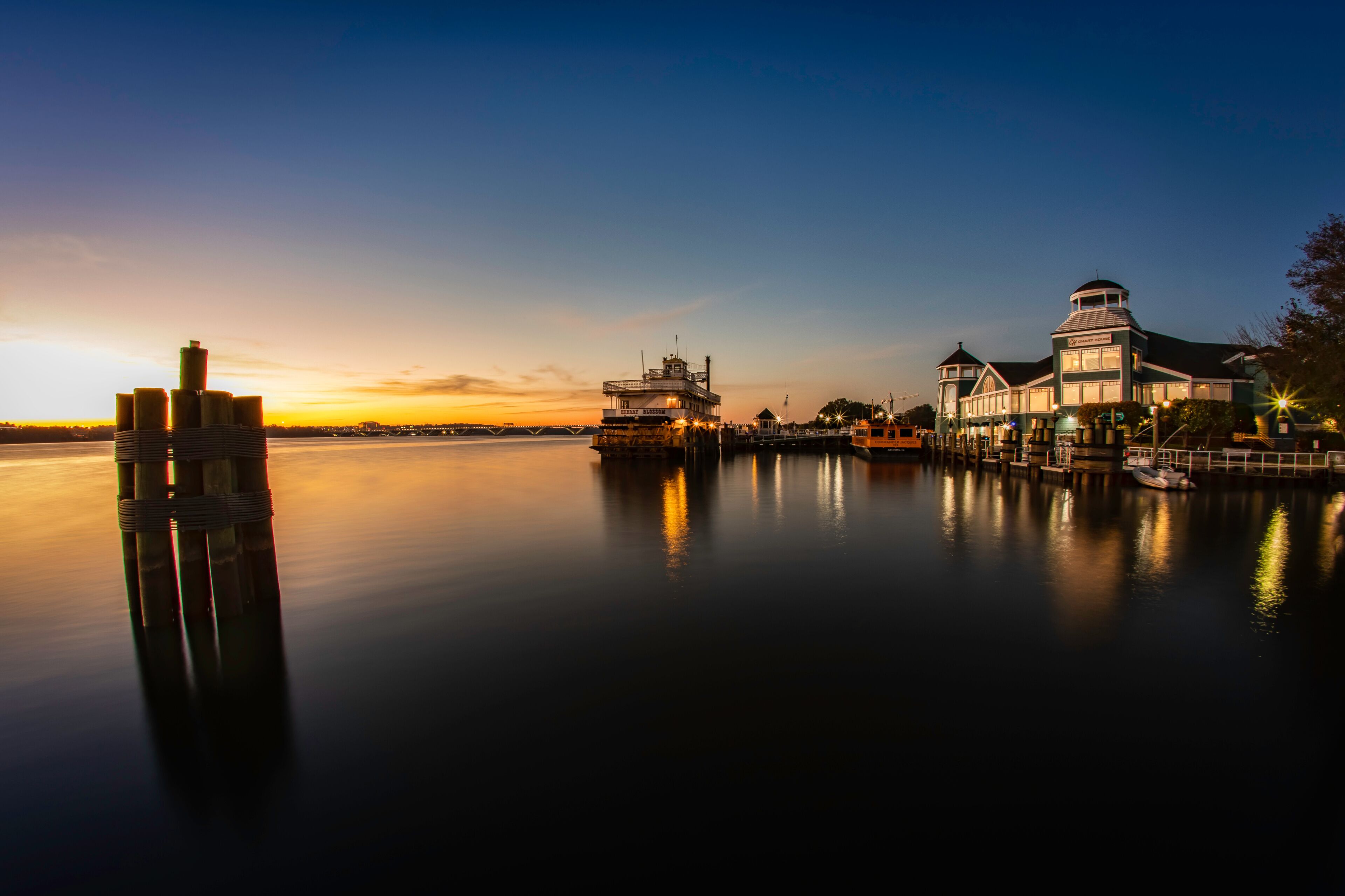 A waterfront with a docked boat, a building with a tower, and a calm sunset.