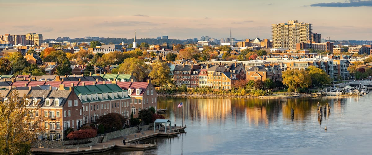 A riverside cityscape with historic buildings, a marina, and a prominent skyscraper.