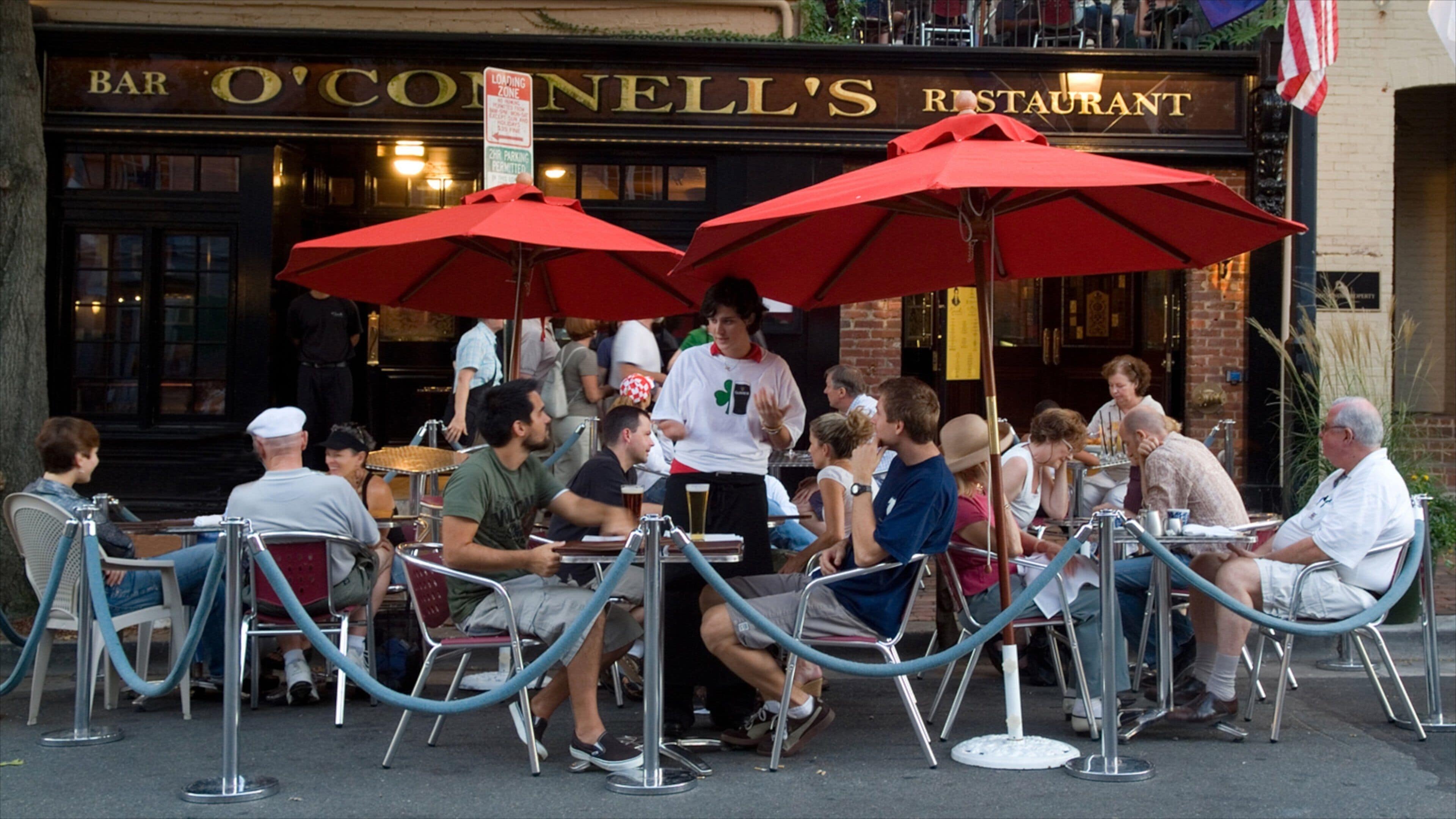 Outdoor seating at Bar O'Connell's Restaurant with red umbrellas and metal stanchions.