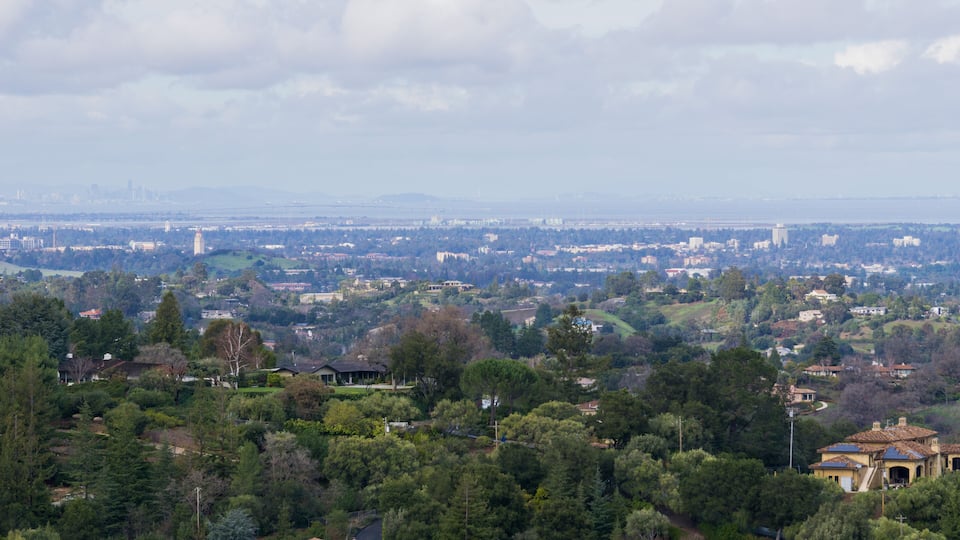 A cityscape with dense residential areas, green spaces, and distant city skyline.