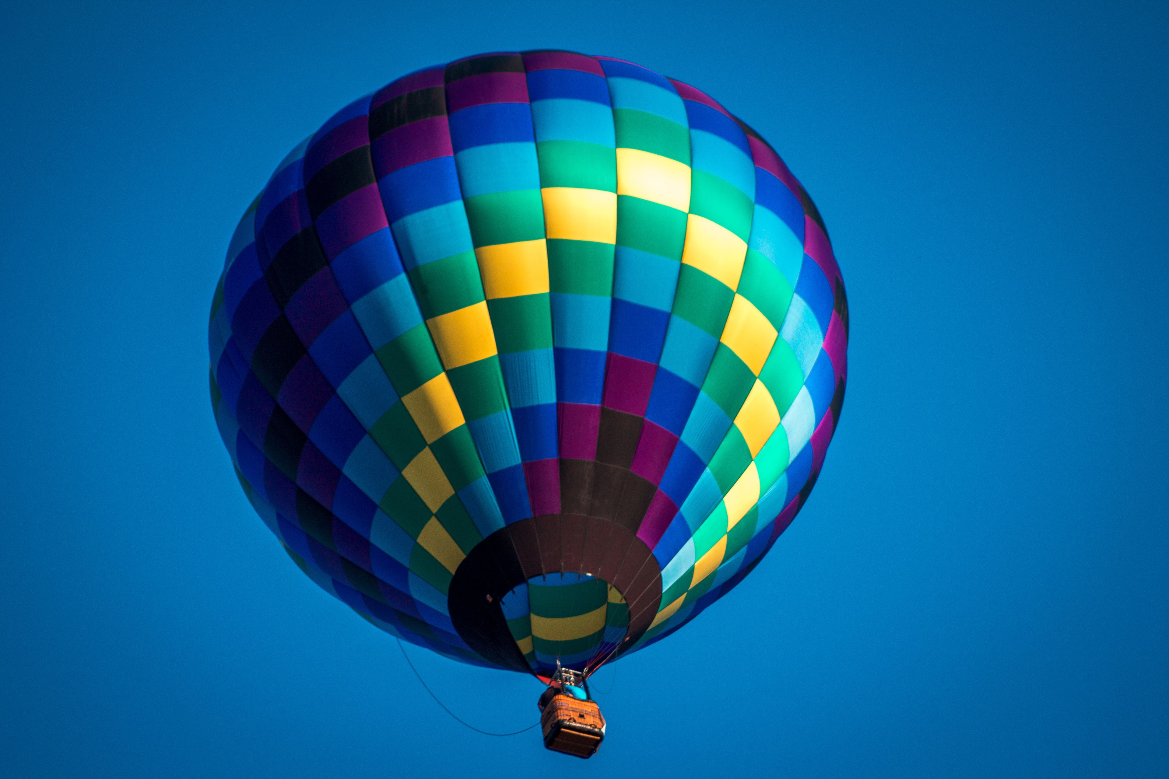 A hot air balloon with a multicolored pattern against a clear blue sky.