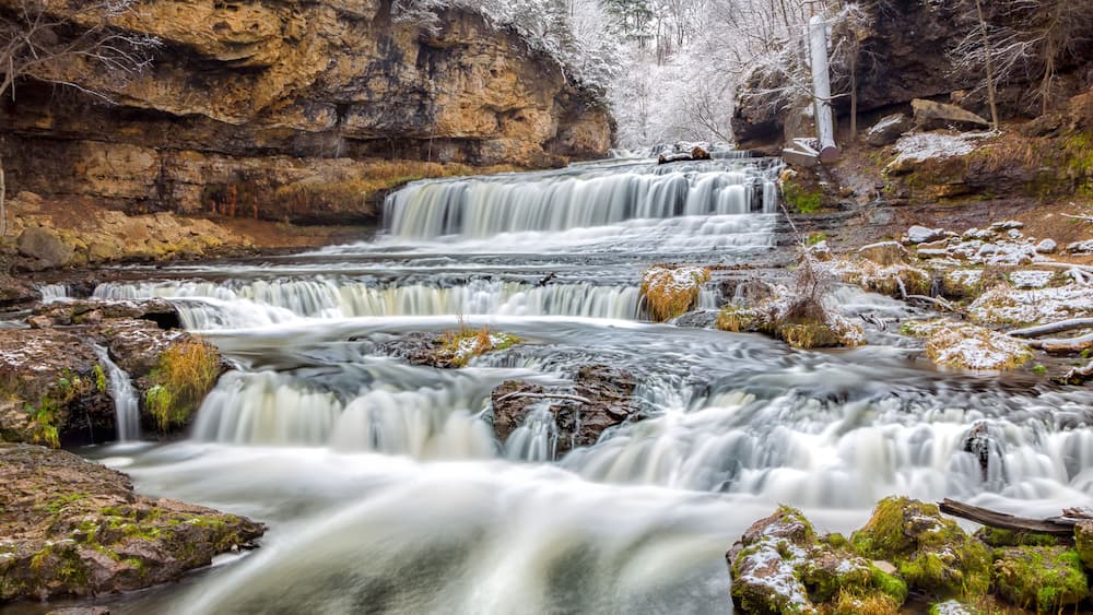 A multi-tiered waterfall surrounded by rocky terrain and sparse vegetation.