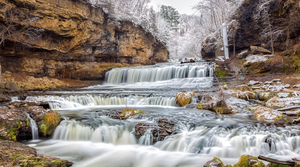 A multi-tiered waterfall surrounded by rocky terrain and sparse vegetation.