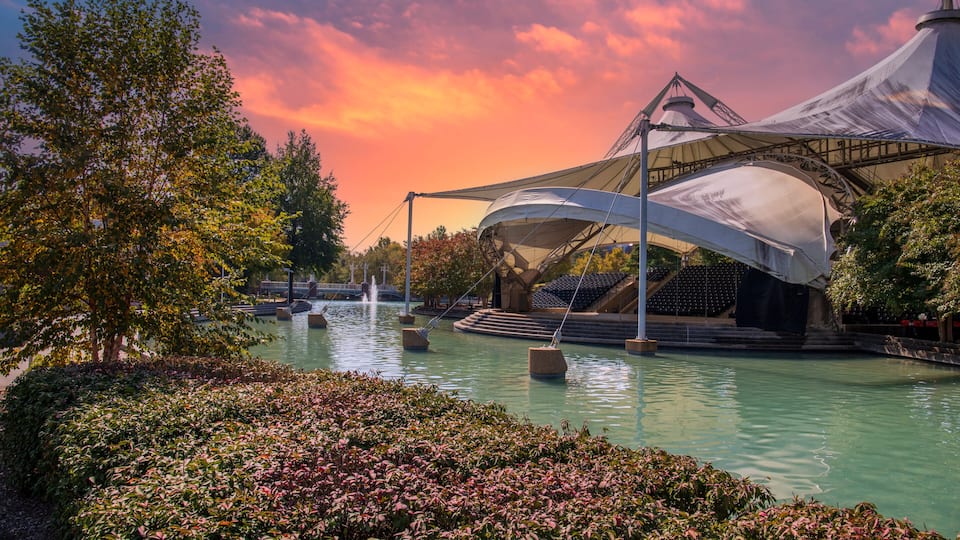 a stunning autumn landscape at World's Fair Park with a pool with blue water surrounded by red and yellow autumn trees and lush green trees and plants with powerful clouds at sunset in Knoxville