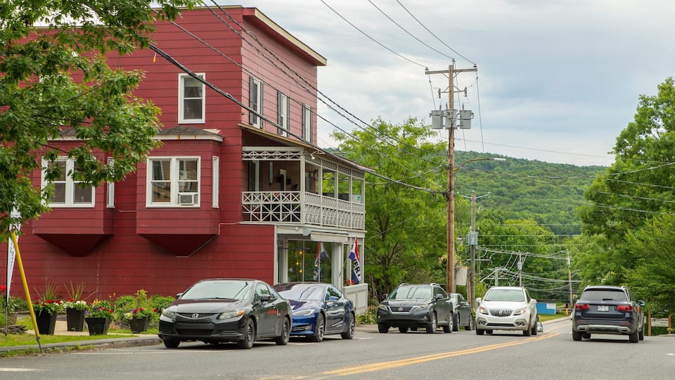 A red building with a balcony, parked cars, and a green hillside in the background.