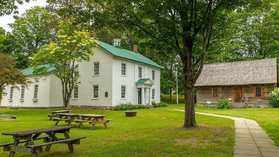 A white building with a green roof, a stone building, picnic tables, and a tree.