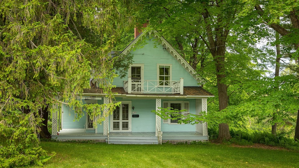 A light blue house with a porch, surrounded by lush greenery and trees.