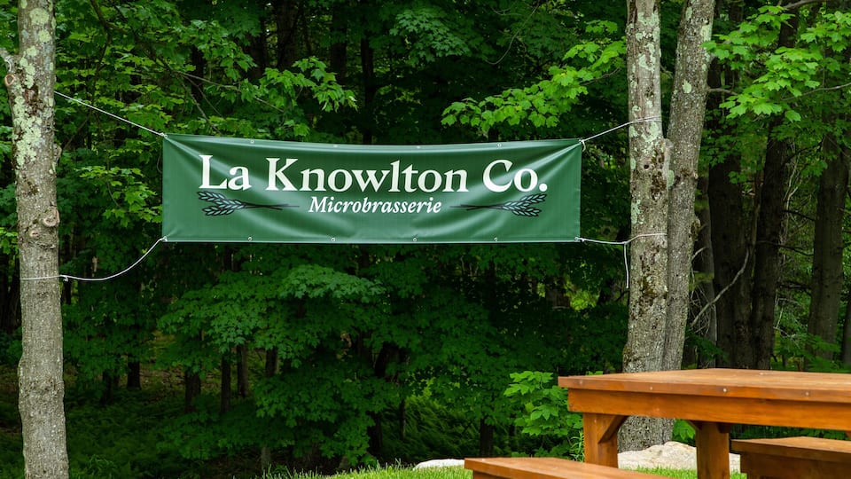 A banner hanging between trees with the text "La Knowlton Co. Microbrasserie".