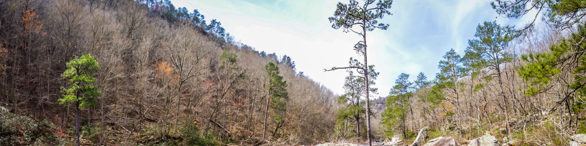 A clear river surrounded by rocky terrain and sparse trees.