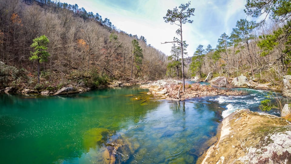 A clear river surrounded by rocky terrain and sparse trees.