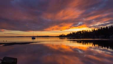 Um pôr do sol sobre um lago calmo, com um veleiro e uma margem arborizada.