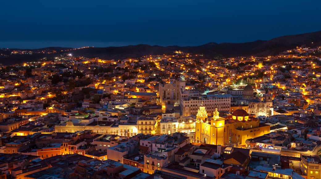 A cityscape at dusk with illuminated buildings and a prominent cathedral with a dome.