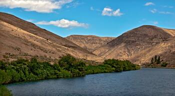 Yakima River Canyon in a panoramic view on a beautiful summer day with blue sky and a scattering of clouds and the river in the foreground. In central Washington.