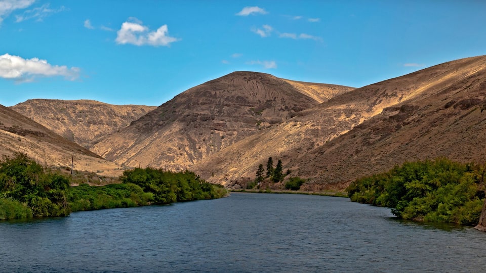 Yakima River Canyon in a panoramic view on a beautiful summer day with blue sky and a scattering of clouds and the river in the foreground. In central Washington.