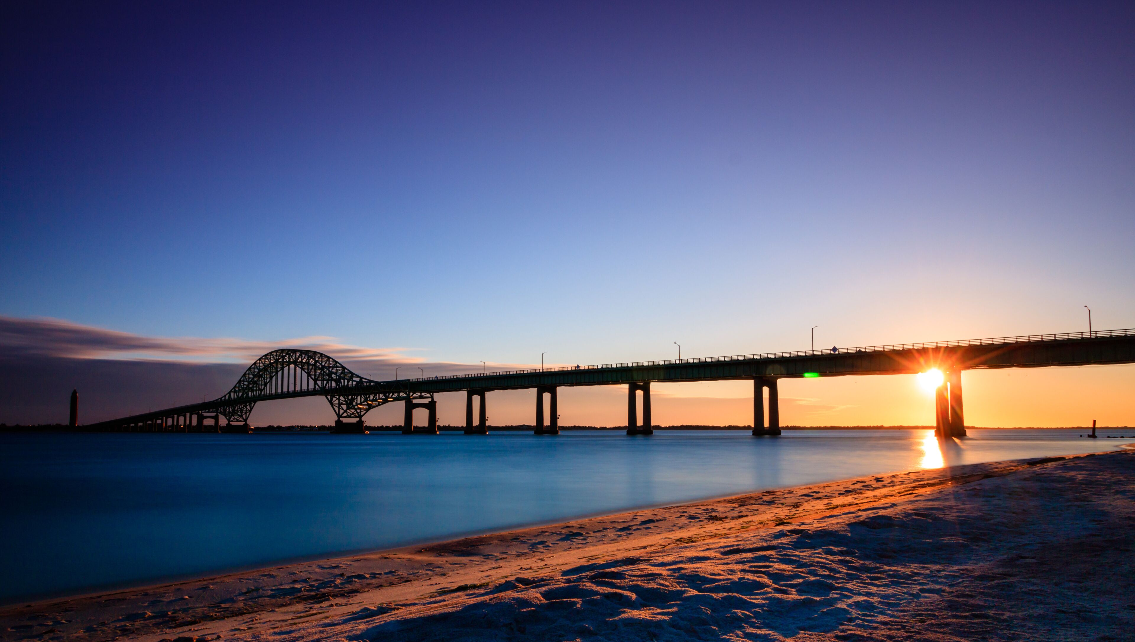 Bridge over glassy smooth water just after sunset, as the last light of the day burns on the horizon. Fire Island Inlet Bridge - Long Island New York. 