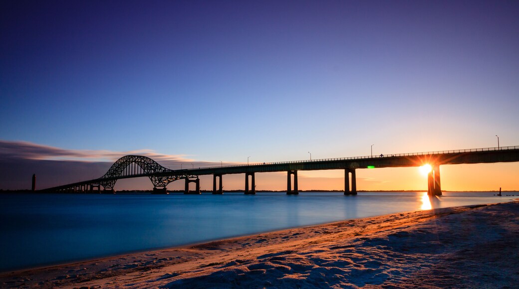 Bridge over glassy smooth water just after sunset, as the last light of the day burns on the horizon. Fire Island Inlet Bridge - Long Island New York.