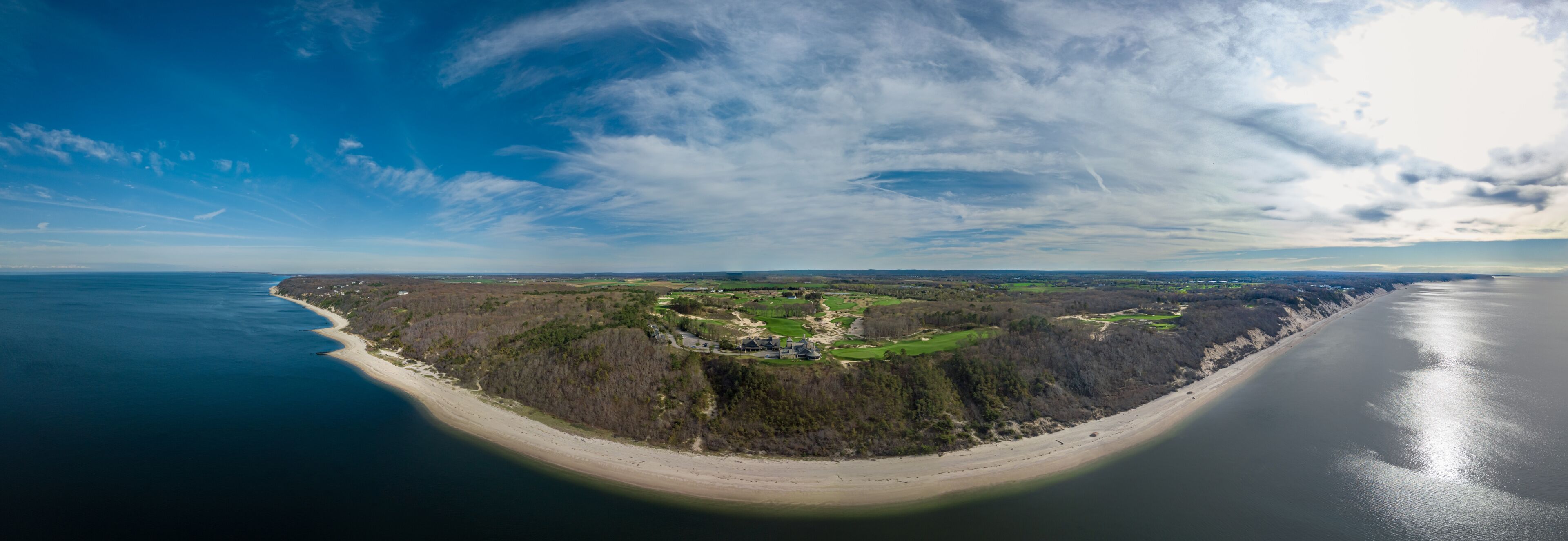 A coastal landscape with a sandy beach, a forested area, and a golf course.