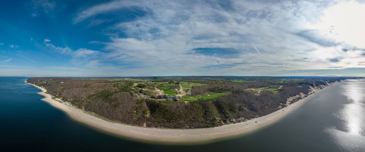 A coastal landscape with a sandy beach, a forested area, and a golf course.