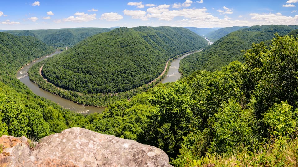 A river winding through a lush valley surrounded by dense forest and rolling hills.