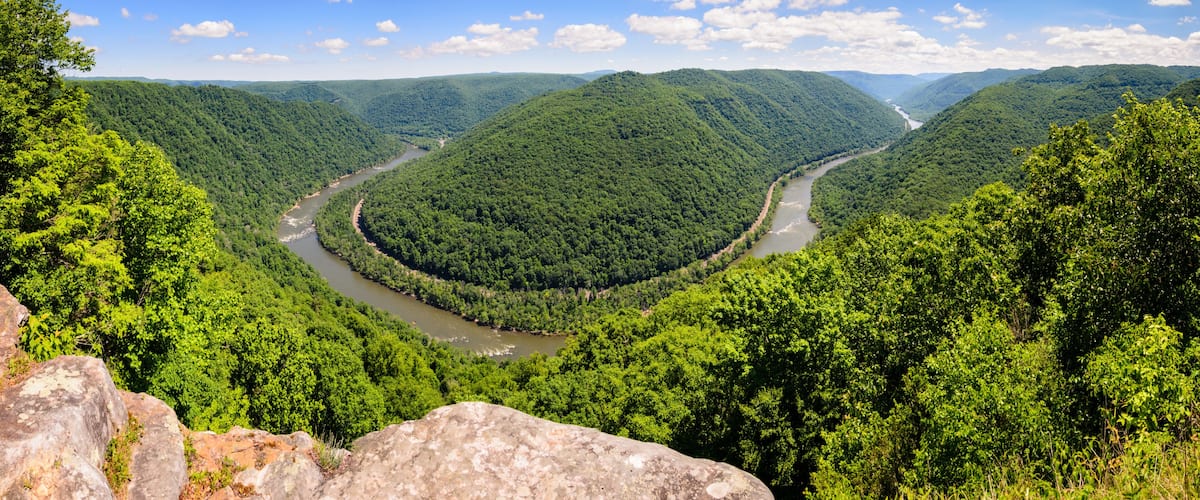 A river winding through a lush valley surrounded by dense forest and rolling hills.