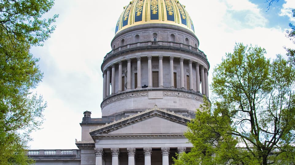The West Virginia State Capitol building with a large dome and a bell in front.