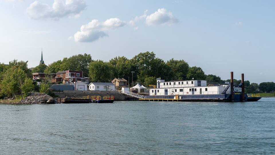 A river with a dock, a white boat, and a church steeple in the background.
