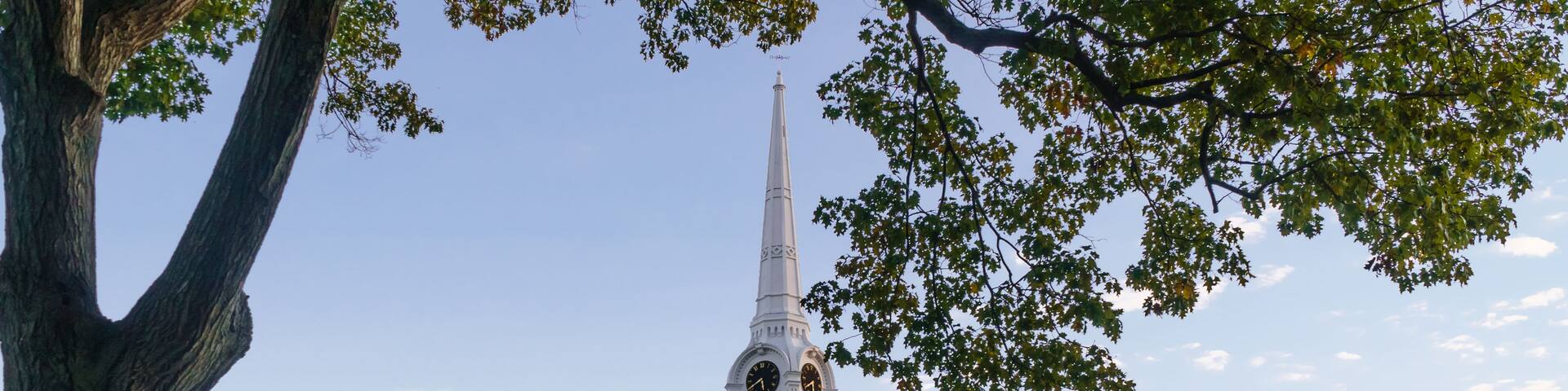 A church with a tall steeple, surrounded by trees and gravestones.