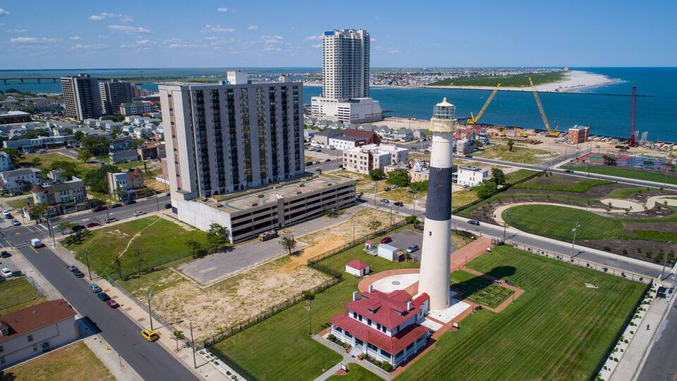 A coastal cityscape with a prominent lighthouse, high-rise buildings, and a bridge in the background.