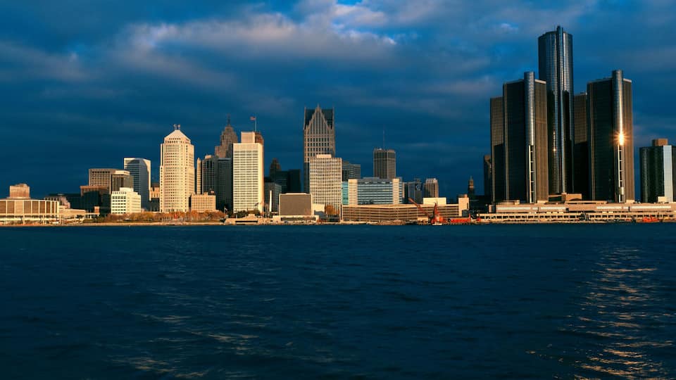 A city skyline with a variety of high-rise buildings, including a distinctive skyscraper with a pointed top, and a waterfront in the foreground.