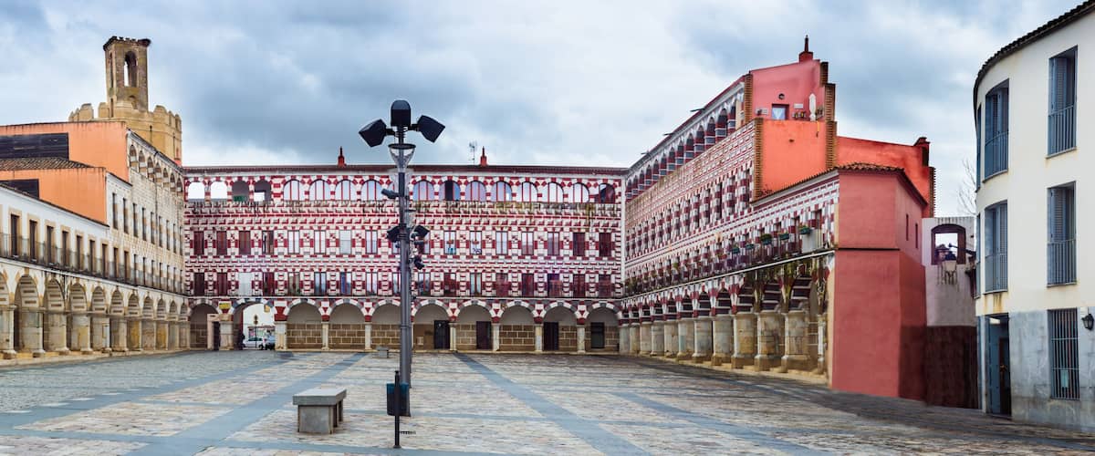 A historic courtyard with a patterned building, a tower, and cobblestone pavement.