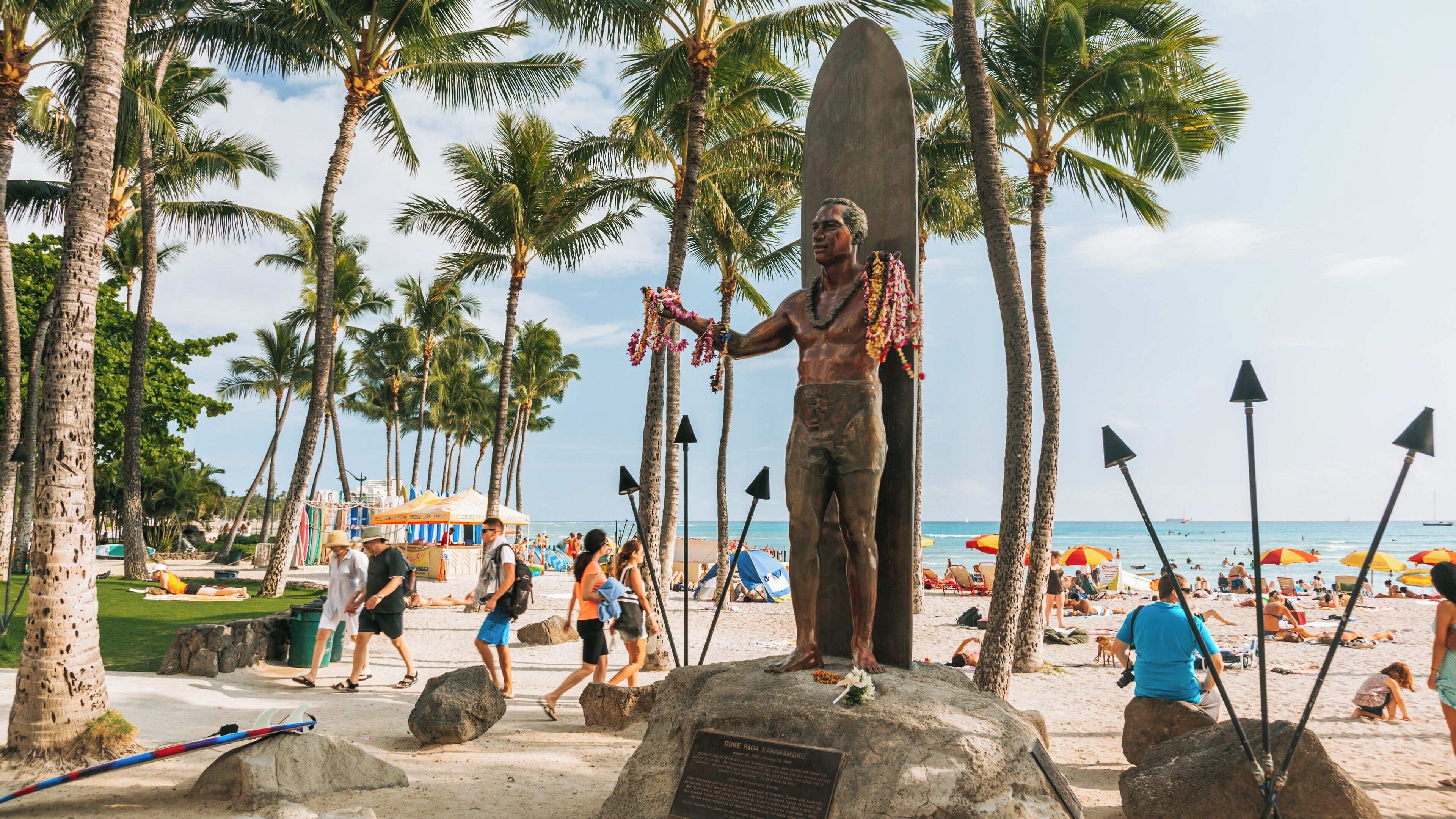 Beautiful day at Waikiki Beach in Honolulu, Hawaii with visitors enjoying the sun and surf near a surfboard statue