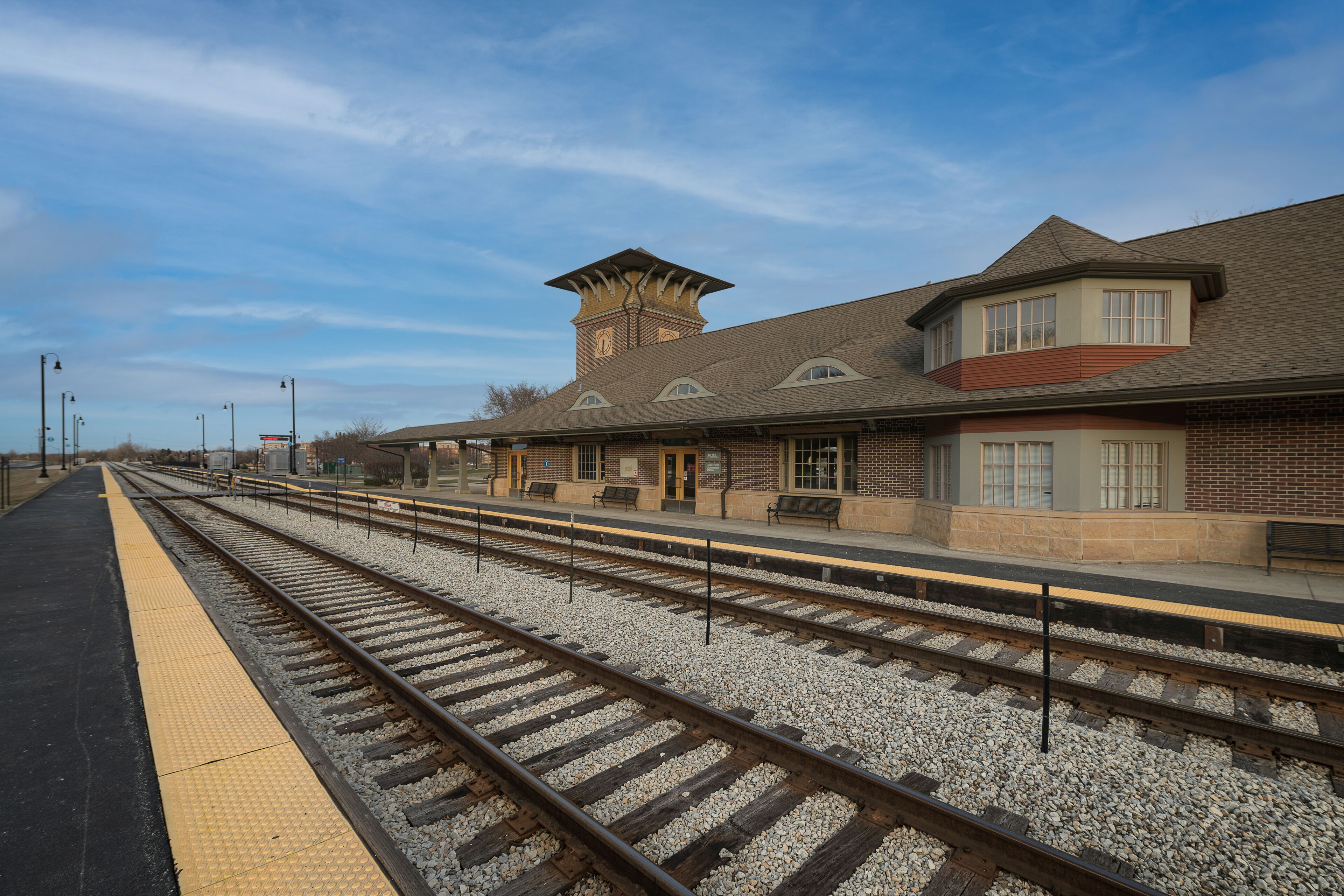 A train station with multiple tracks, a clock tower, and benches along the platform.