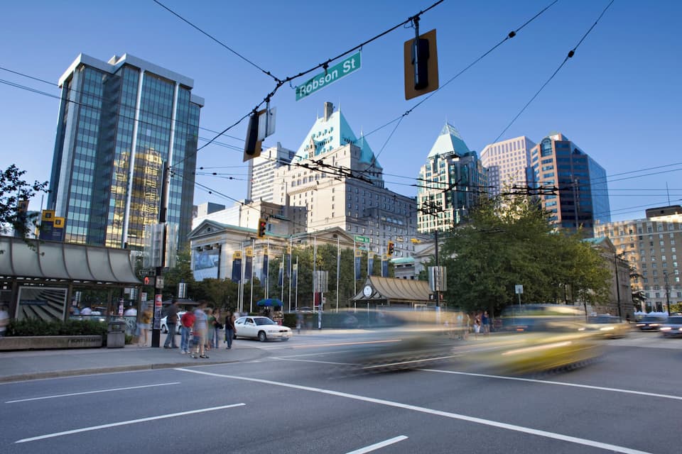 A city intersection with Robson St sign, modern buildings, and a historic building with a clock tower.