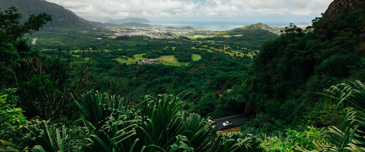 A lush valley with mountains in the background, a winding road, and a small building in the foreground.