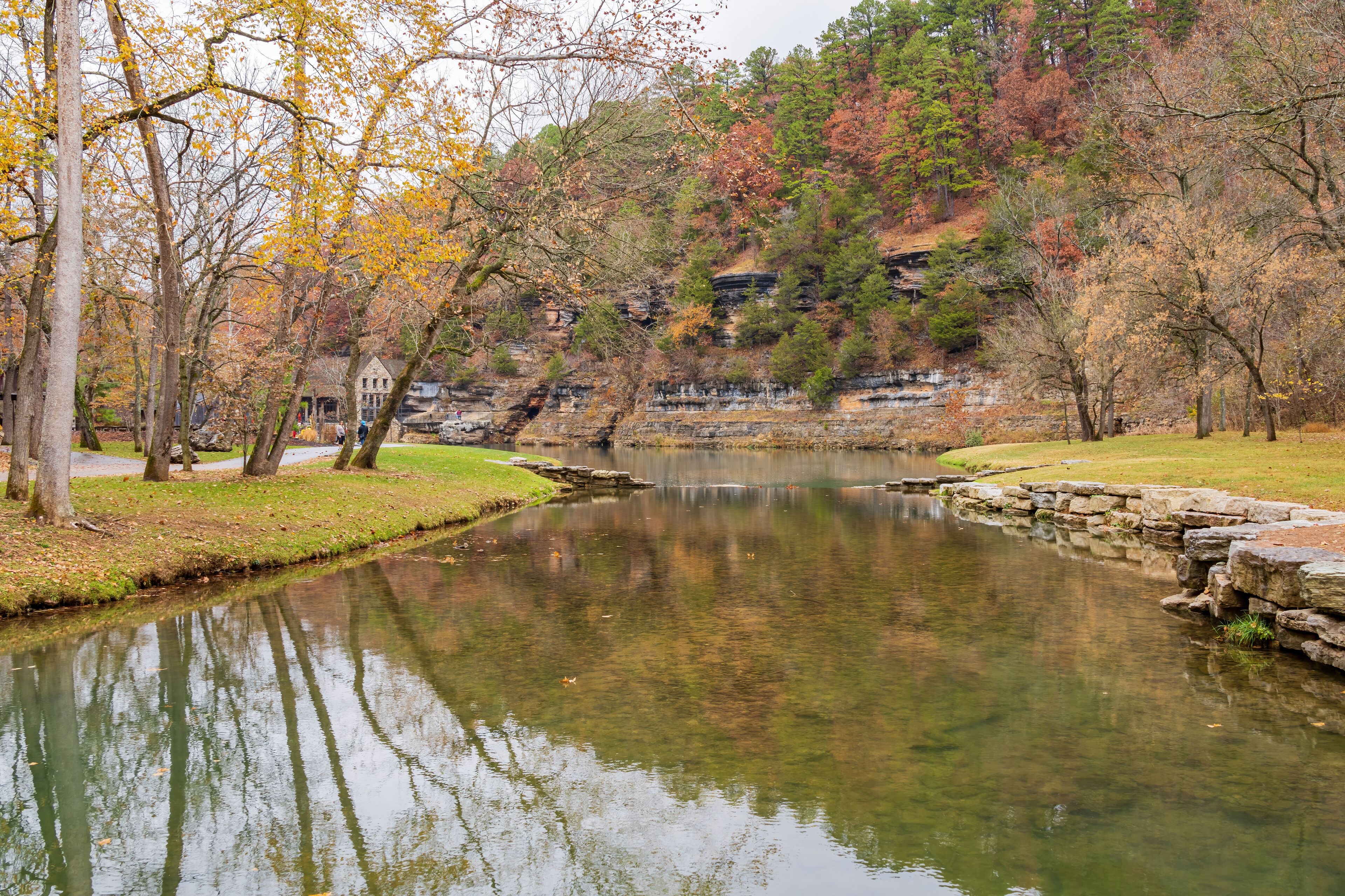 A calm river with autumn foliage, a stone bridge, and a building in the background.