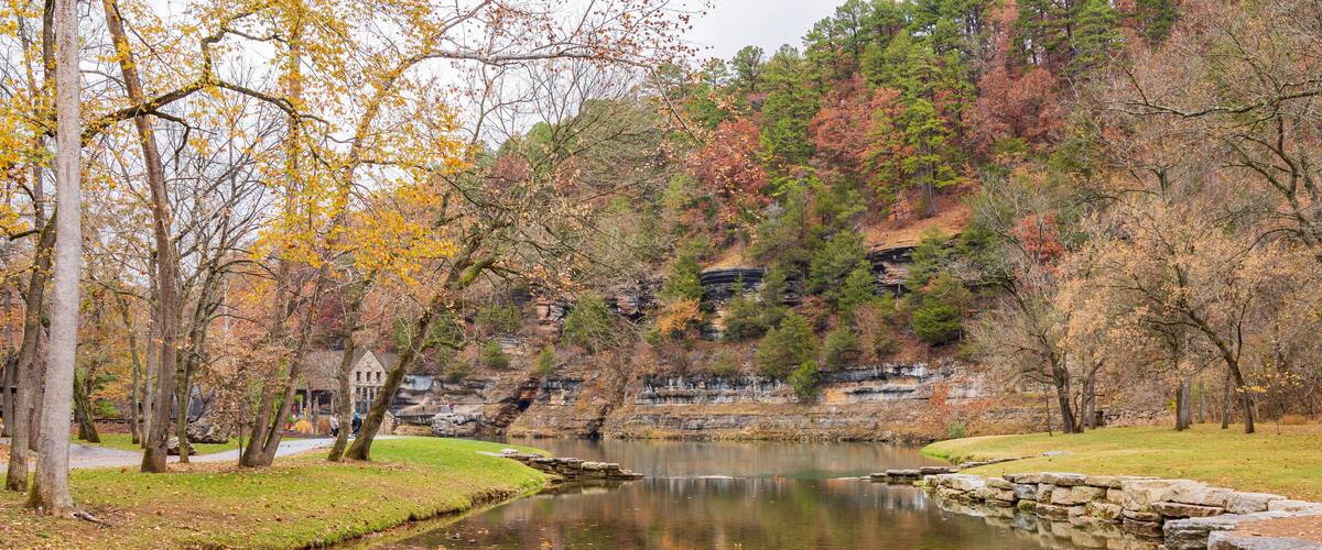 A calm river with autumn foliage, a stone bridge, and a building in the background.
