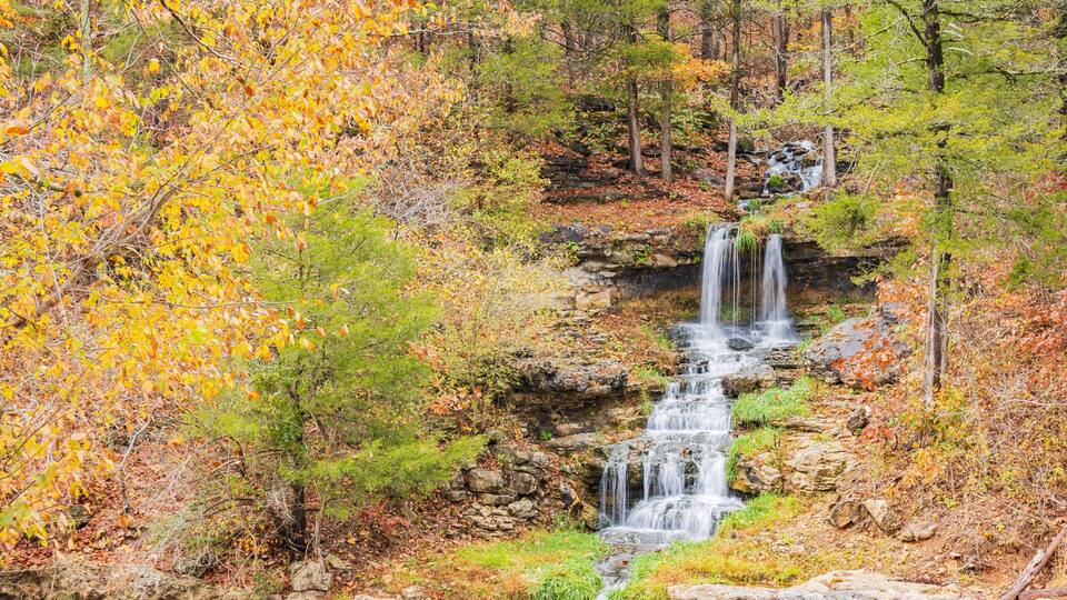 A waterfall cascading down a rocky slope surrounded by autumn foliage.