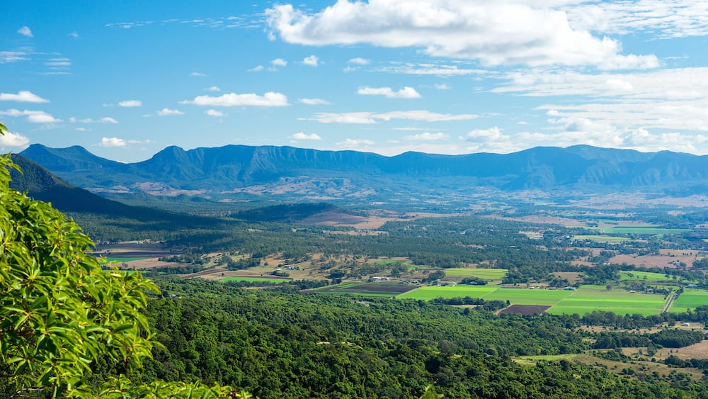 Eine Berglandschaft mit einem Tal, grünen Feldern und verstreuten Gebäuden.