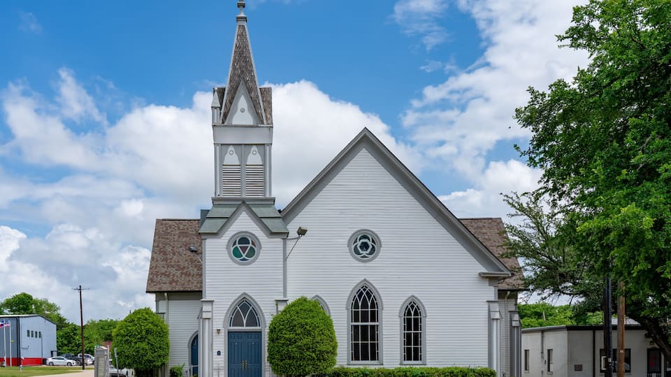 A white church with a steeple, a blue door, and a small tree in front.