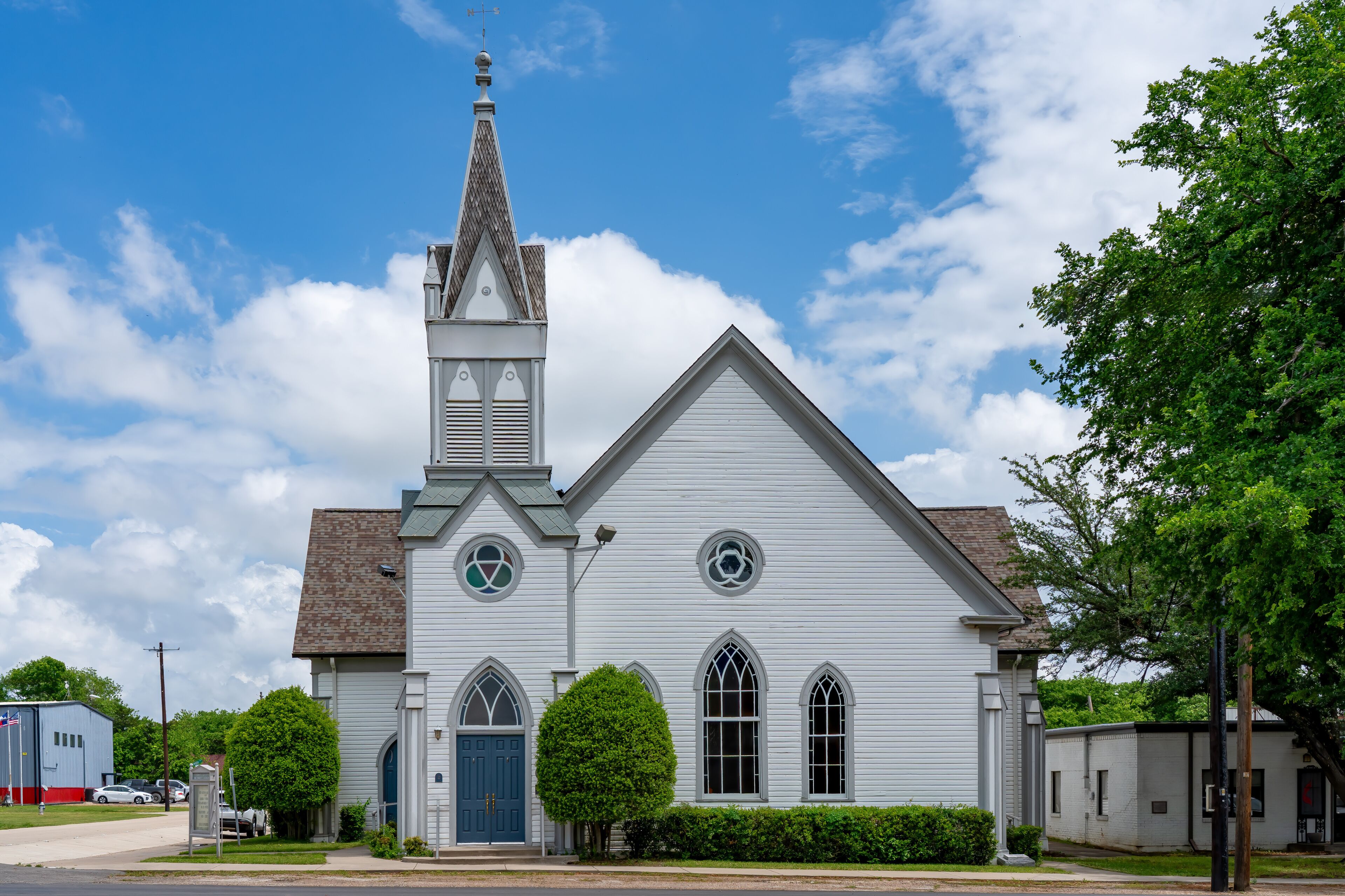A white church with a steeple, a blue door, and a small tree in front.
