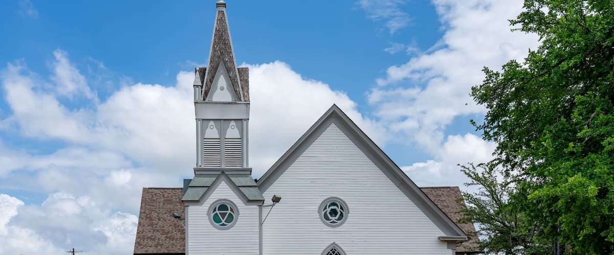 A white church with a steeple, a blue door, and a small tree in front.