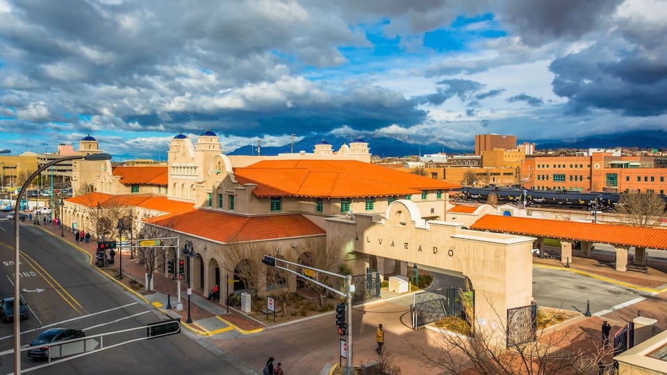A cityscape with historic buildings, a train station, and a mountainous backdrop.