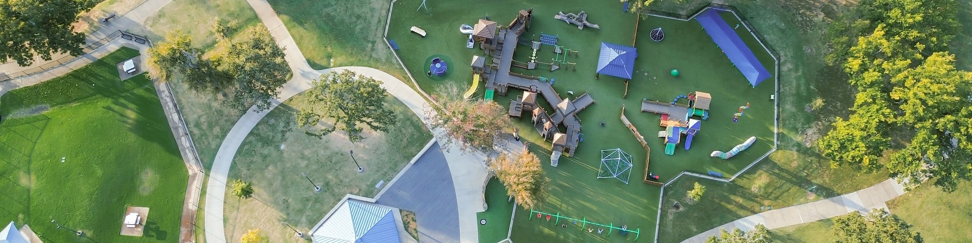 An aerial view of a park with playground equipment, a soccer field, and a small building.