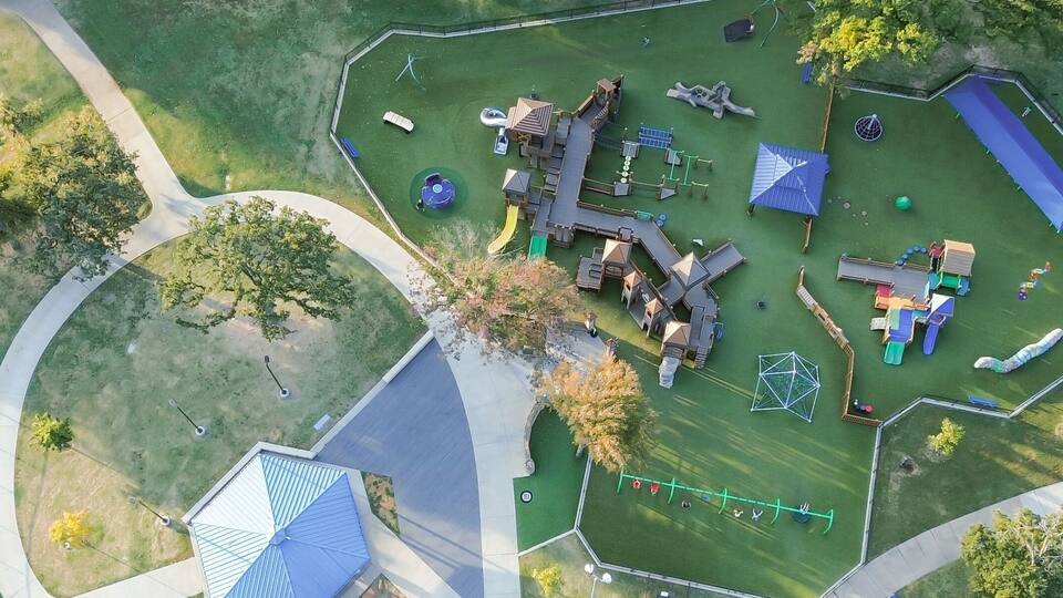An aerial view of a park with playground equipment, a soccer field, and a small building.