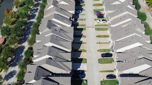 Panorama aerial canal with bridge, waterfall, flat roof restaurant, parking garage next row of suburban homes gabled roofs, integration of residential living, commercial zones, Flower Mound, TX