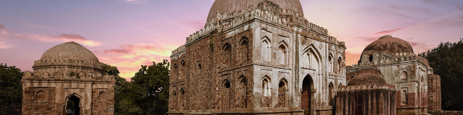 A historical building with a large central dome and smaller domes, surrounded by a grassy area.