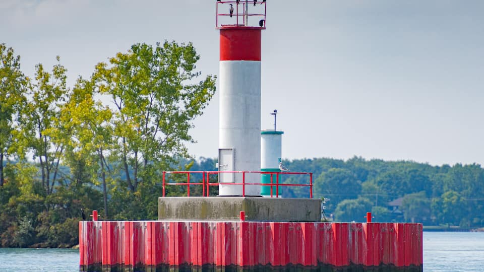 A lighthouse on a red pier with a white tower, surrounded by water and trees.